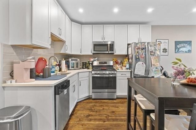 kitchen with appliances with stainless steel finishes, a sink, light countertops, dark wood-type flooring, and white cabinets
