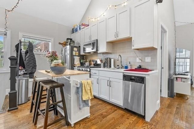 kitchen featuring appliances with stainless steel finishes, a sink, light wood finished floors, decorative backsplash, and high vaulted ceiling