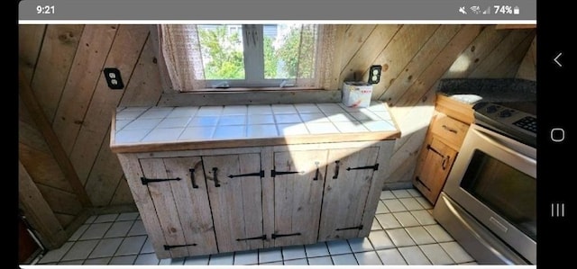 kitchen featuring tile countertops, wooden walls, light tile patterned floors, and range