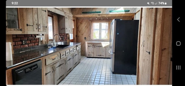 kitchen with wood walls, sink, light tile patterned floors, black dishwasher, and stainless steel refrigerator