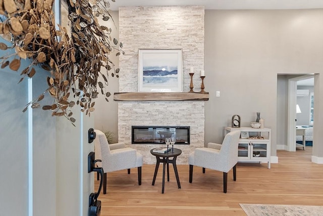 sitting room with baseboards, wood finished floors, and a stone fireplace