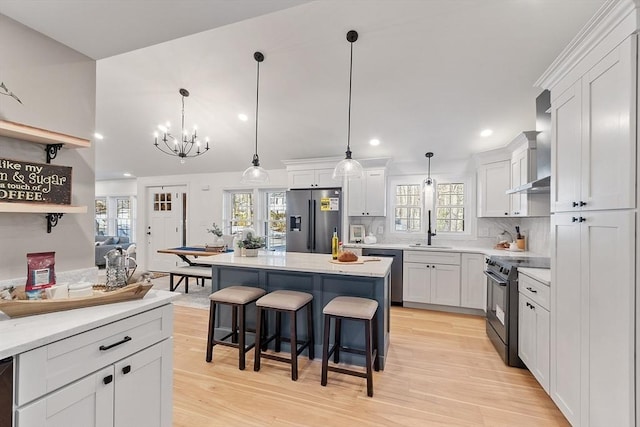 kitchen featuring stainless steel appliances, white cabinets, a sink, wall chimney range hood, and a kitchen bar