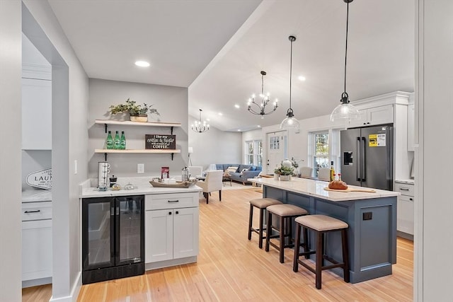 kitchen featuring wine cooler, light wood finished floors, white cabinetry, stainless steel fridge, and a kitchen breakfast bar