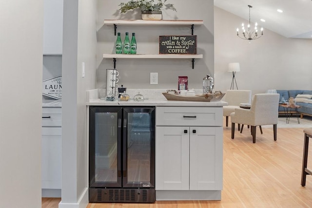 bar with a dry bar, light wood finished floors, beverage cooler, and a chandelier