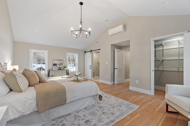 bedroom featuring light wood-style flooring, a spacious closet, a wall mounted AC, a barn door, and vaulted ceiling