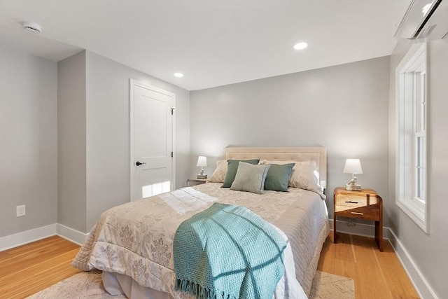 bedroom with a wall mounted AC, wood finished floors, and baseboards