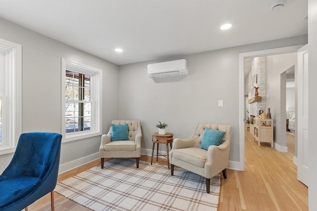 sitting room with a wall mounted AC, recessed lighting, light wood-style flooring, and baseboards