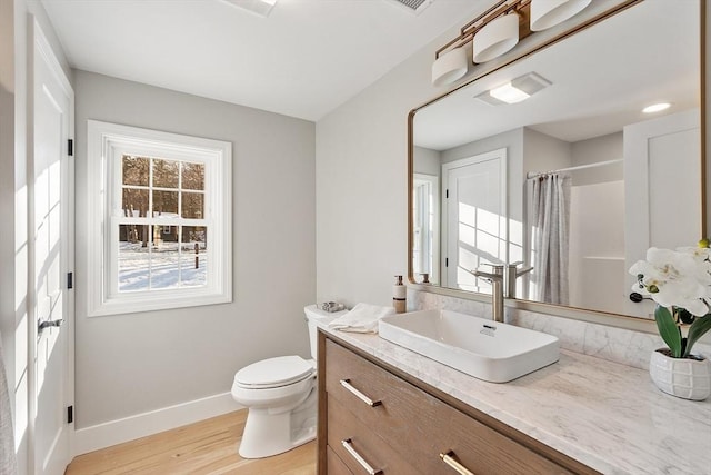 bathroom with a shower with shower curtain, toilet, vanity, wood finished floors, and baseboards