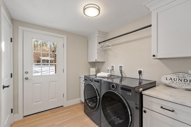 laundry area with light wood-type flooring, cabinet space, baseboards, and washer and dryer