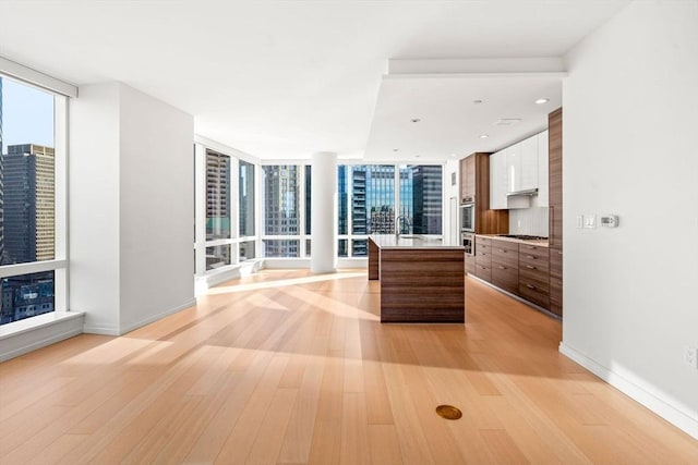 kitchen featuring a center island, gas stovetop, expansive windows, white cabinets, and light wood-type flooring