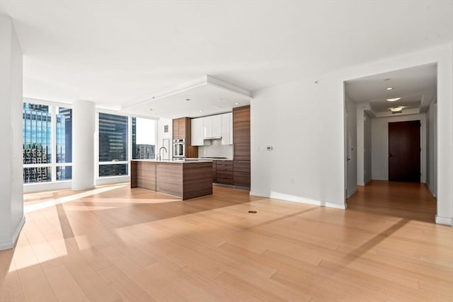 kitchen featuring floor to ceiling windows, stainless steel oven, sink, a center island with sink, and light wood-type flooring