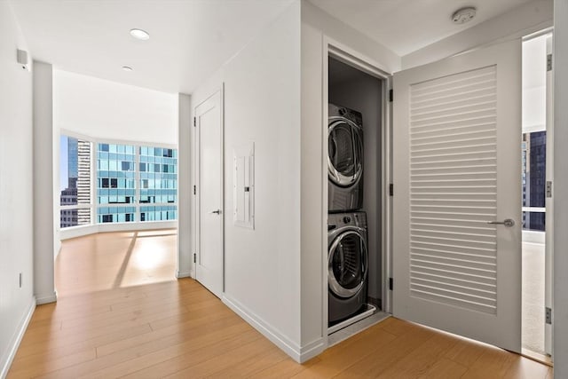 clothes washing area featuring stacked washer / dryer, electric panel, and light wood-type flooring