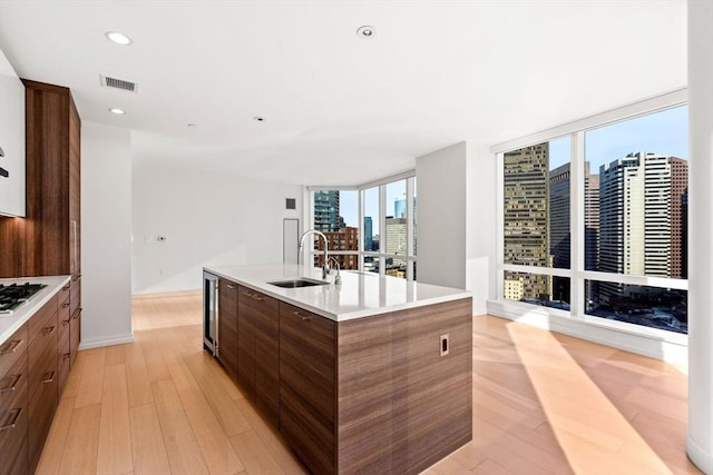 kitchen featuring floor to ceiling windows, gas stovetop, sink, a center island with sink, and light hardwood / wood-style floors