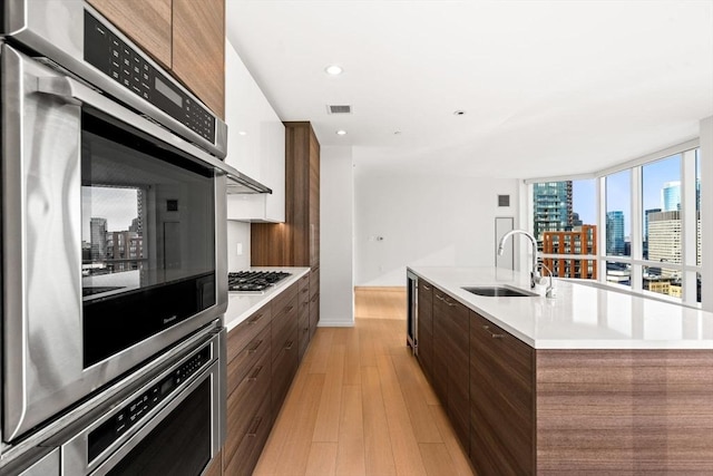 kitchen with a center island with sink, light wood-type flooring, sink, and appliances with stainless steel finishes