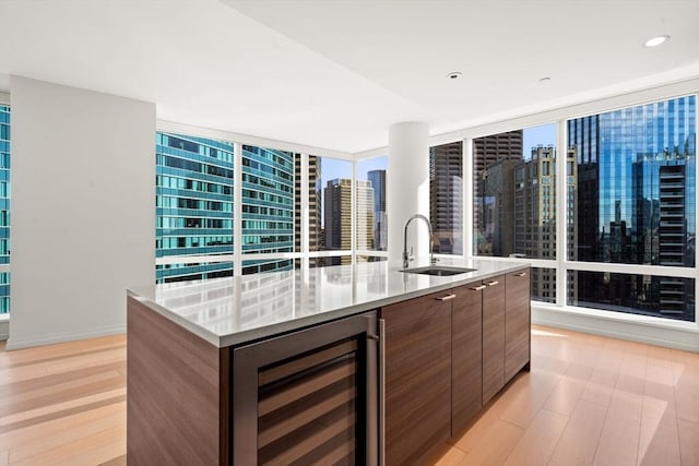 kitchen featuring light wood-type flooring, floor to ceiling windows, sink, a center island with sink, and wine cooler