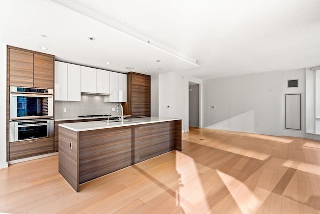 kitchen with white cabinetry, stainless steel double oven, gas cooktop, light hardwood / wood-style flooring, and backsplash