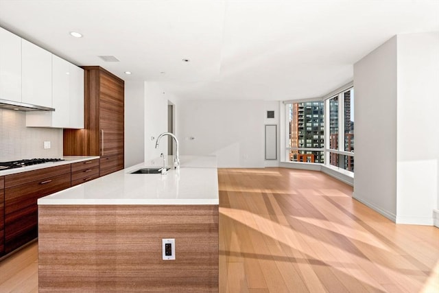 kitchen with gas cooktop, tasteful backsplash, a kitchen island with sink, sink, and white cabinetry