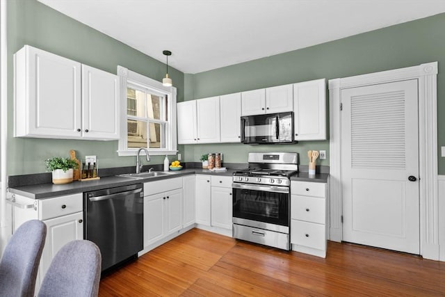 kitchen with pendant lighting, sink, white cabinetry, stainless steel appliances, and wood-type flooring