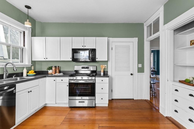 kitchen with sink, white cabinetry, wood-type flooring, black appliances, and decorative light fixtures