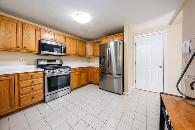 kitchen with stainless steel appliances, light tile patterned flooring, light countertops, and brown cabinets