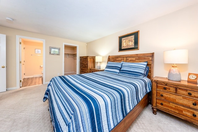 bedroom with a walk in closet, a closet, light colored carpet, connected bathroom, and baseboards