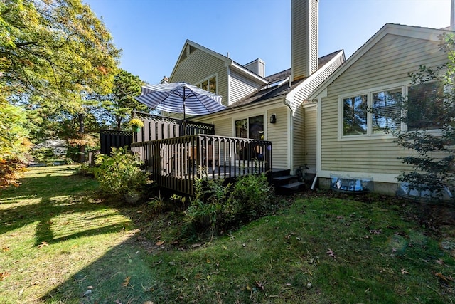 rear view of property with a chimney, a yard, and a deck