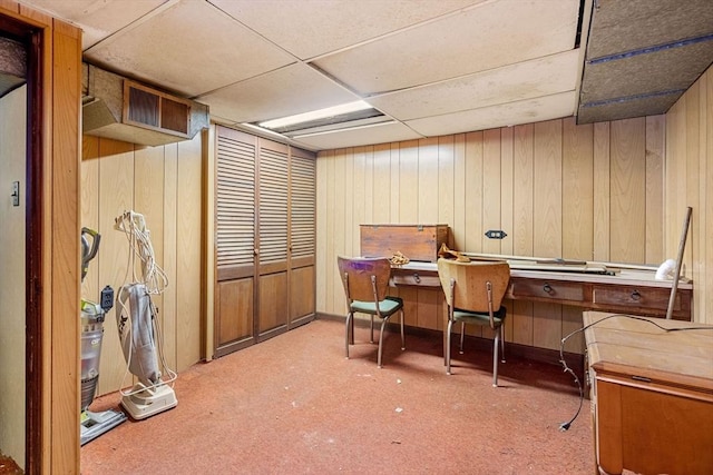 carpeted home office with a paneled ceiling and wooden walls