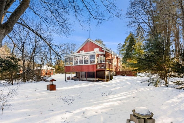 snow covered rear of property with a sunroom