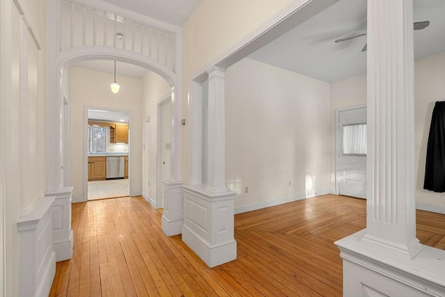 corridor featuring light wood finished floors, decorative columns, arched walkways, and baseboards