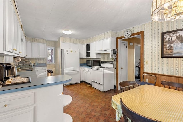 kitchen featuring hanging light fixtures, white cabinets, wainscoting, white appliances, and wallpapered walls