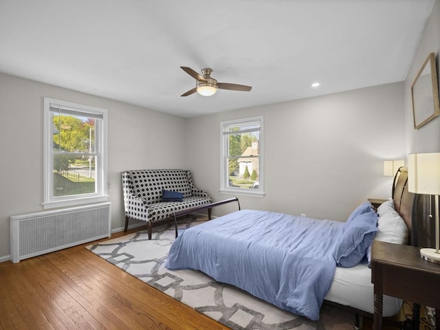 bedroom with radiator, multiple windows, wood-type flooring, and baseboards