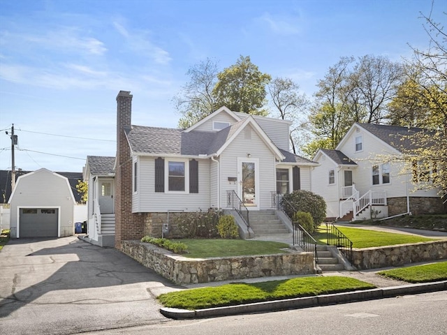 bungalow-style house with a front lawn, aphalt driveway, a garage, an outbuilding, and a chimney