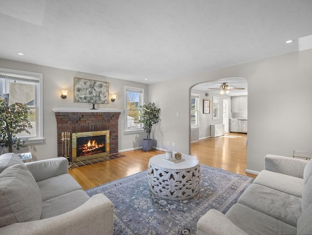 living room with arched walkways, ceiling fan, a fireplace, and wood finished floors