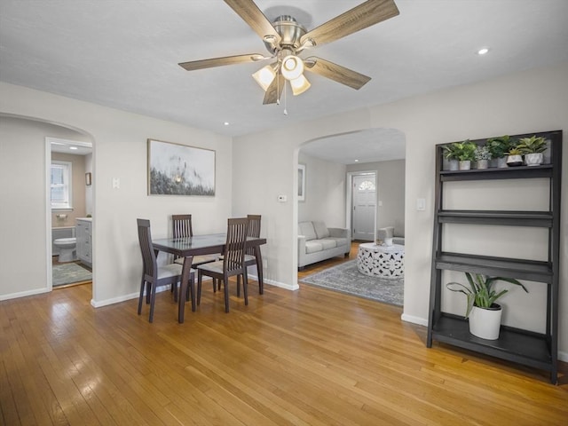 dining room with light wood-type flooring, arched walkways, baseboards, and ceiling fan
