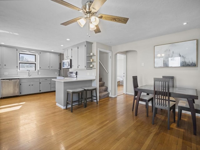 dining room featuring arched walkways, a ceiling fan, stairway, and light wood-style floors