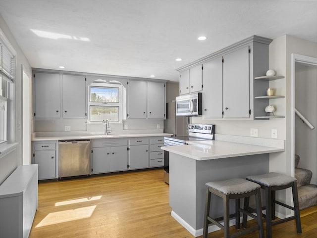 kitchen with a sink, gray cabinets, a peninsula, and stainless steel appliances