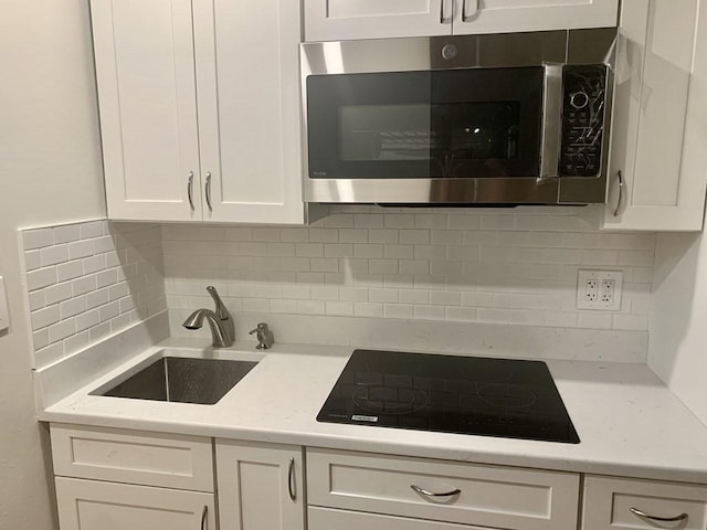 kitchen with stainless steel microwave, a sink, black electric cooktop, white cabinets, and decorative backsplash