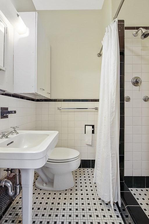 full bath with toilet, a shower stall, tile walls, and wainscoting