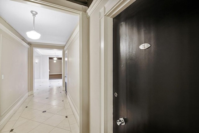 hallway featuring light tile patterned floors, ornamental molding, and baseboards