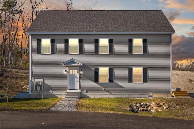 colonial-style house featuring entry steps, a front yard, and a shingled roof