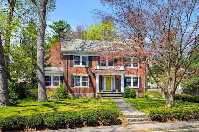 colonial inspired home featuring brick siding, a front lawn, and a chimney