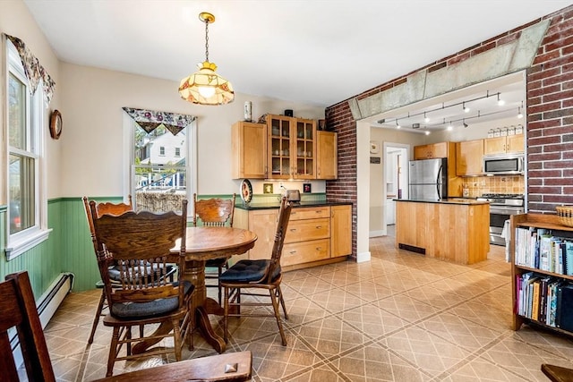 dining room featuring rail lighting, a baseboard heating unit, a healthy amount of sunlight, and a wainscoted wall