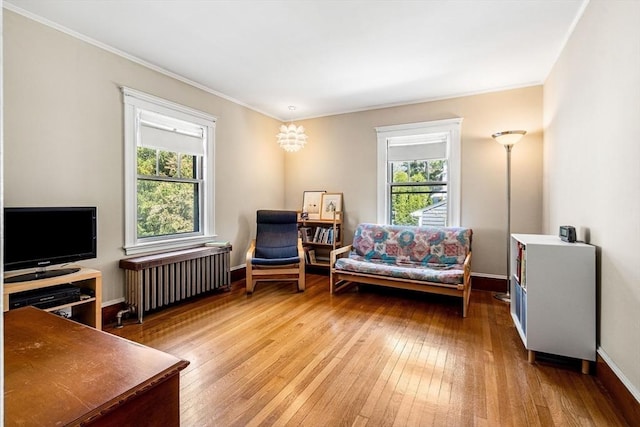 sitting room featuring crown molding, baseboards, light wood-style floors, and radiator heating unit