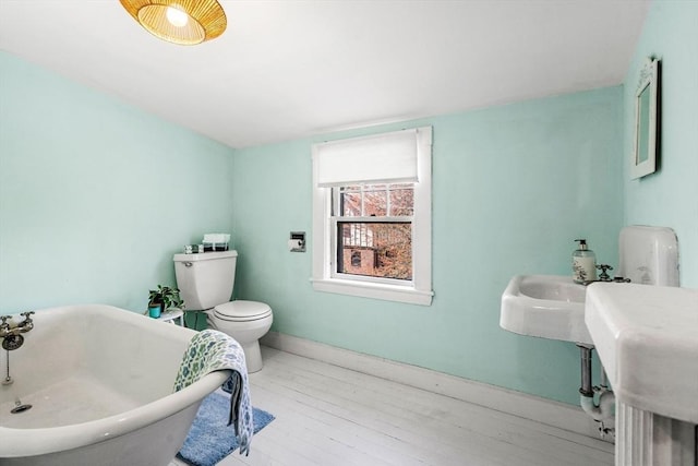 bathroom with toilet, baseboards, a freestanding bath, and wood finished floors