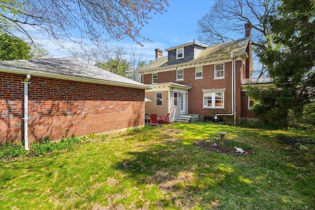 rear view of property featuring brick siding, a lawn, and a chimney