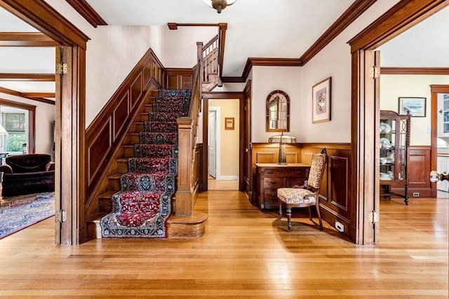 staircase with a decorative wall, ornamental molding, wainscoting, and hardwood / wood-style floors