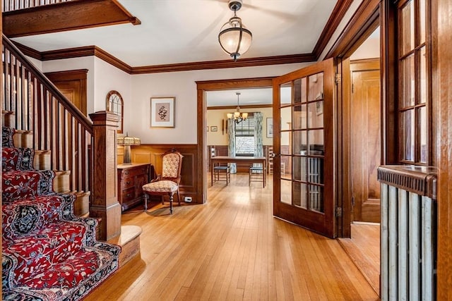entryway with wood-type flooring, crown molding, wainscoting, stairway, and a chandelier