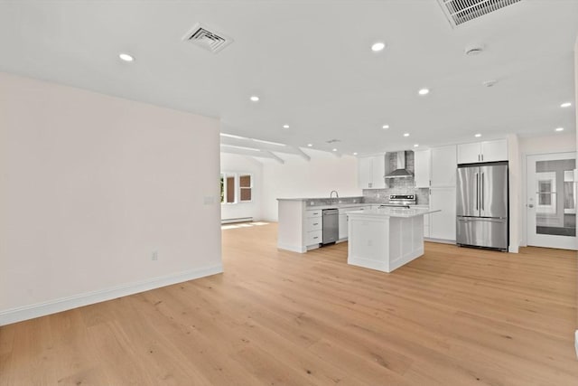 kitchen featuring stainless steel appliances, wall chimney range hood, open floor plan, light wood-type flooring, and baseboards