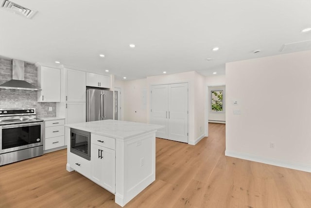 kitchen with wall chimney range hood, appliances with stainless steel finishes, backsplash, white cabinets, and light wood-style floors