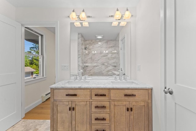 full bathroom with a marble finish shower, a baseboard heating unit, double vanity, baseboards, and wood finished floors